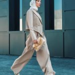 Elegant woman wearing a beige suit and headscarf walking by a modern building.